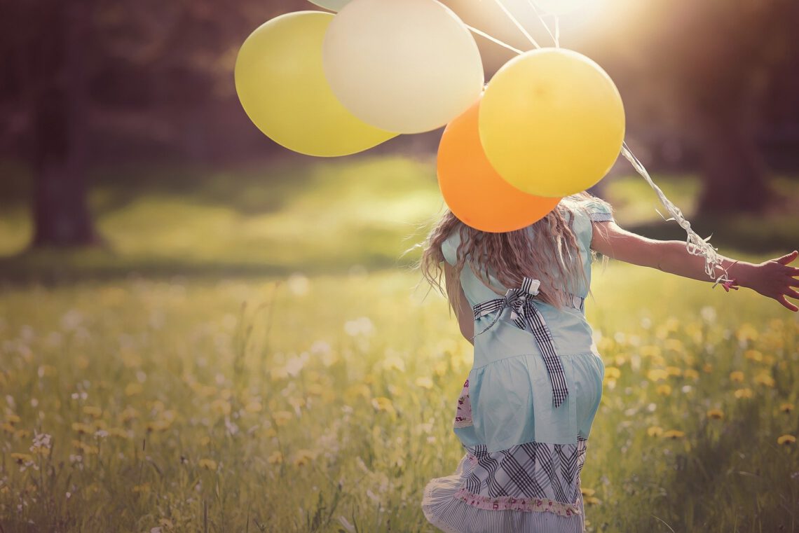 Mädchen rennt mit Luftballons über eine Wiese