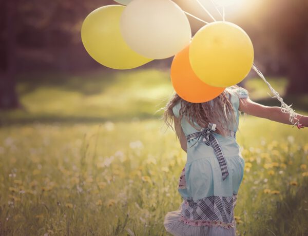 Mädchen rennt mit Luftballons über eine Wiese